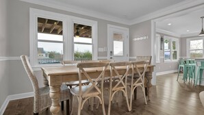 Un espace repas avec une table et des chaises en bois, de grandes fenêtres et une vue sur l’extérieur.