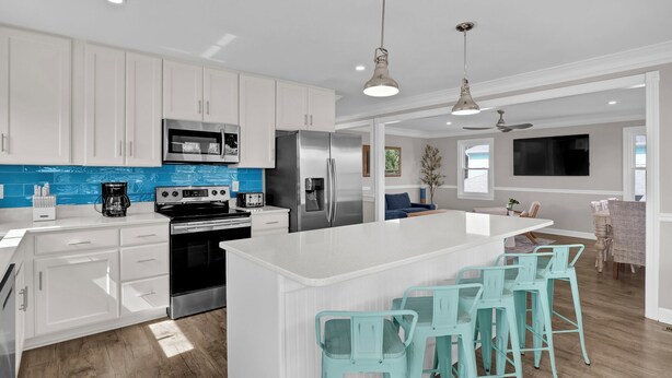 Une cuisine moderne avec des meubles blancs, un îlot central doté de tabourets de bar, des appareils en acier inoxydable et un pare-feu bleu.