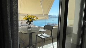 A balcony with a table and chair, a vase with yellow flowers, and a view of the sea and distant buildings. - Italian design apartment for a refined explorer of new destinations. (Saranda)