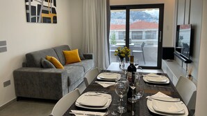 A modern dining area with a table set for four, a grey sofa with yellow cushions, and a city view through the window. - Italian design apartment for a refined explorer of new destinations. (Saranda)