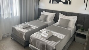 A modern hotel room with two beds, a grey upholstered headboard, a bedside table with a plant, and a large abstract painting on the wall. - Italian design apartment for a refined explorer of new destinations. (Saranda)