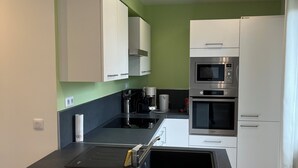 Une cuisine moderne avec des armoires blanches, un plan de travail noir et des appareils en acier inoxydable, notamment un four à micro-ondes et un four traditionnel.