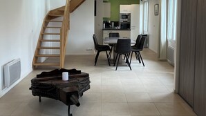 Un vaste espace de vie agrémenté d’un escalier en bois, d’une table à manger avec des chaises, et d’une cuisine située au fond de la pièce.