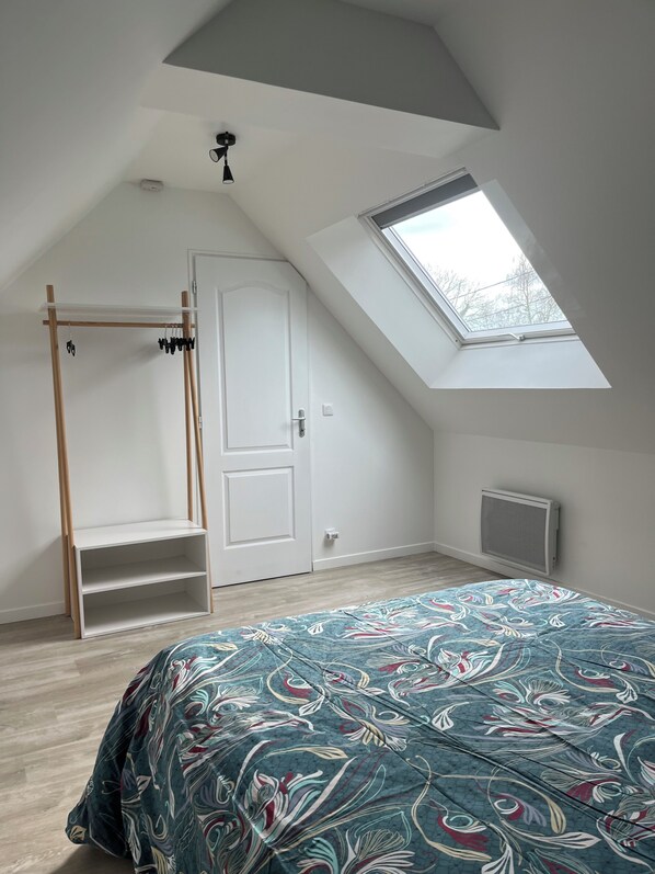 Ein Schlafzimmer mit schrägen Wänden, einem Oberlicht, einem weißen Kleiderschrank, einer Holzregaleinheit und einer geblümten Bettdecke.
