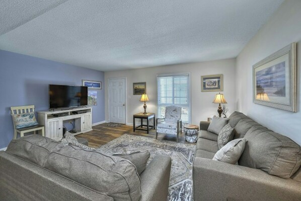 A living room with a television, two armchairs, a sofa, a small table, and a lamp.