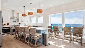 A modern kitchen with a large island, bar stools, and a view of the ocean.