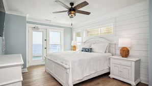 A bedroom with a bed, nightstands, a ceiling fan, and a view of the ocean.