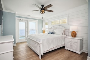 A bedroom with a bed, nightstands, a ceiling fan, and a view of the ocean.