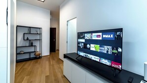 A modern living room with a flat-screen TV mounted on a black TV stand, a white cabinet below, and a wooden floor. - Luxury apartment 300 meters from Milan Cathedral and Piazza San Babila (Milano)