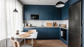 A modern kitchen with blue cabinets, a black refrigerator, and a dining area with a white table and chairs.