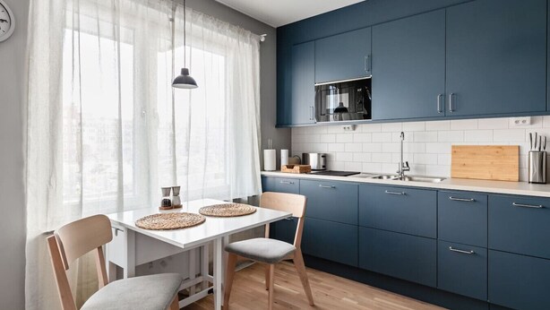 A modern kitchen with dark blue cabinets, a white countertop, and a dining area with two chairs and a table.