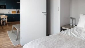A modern bedroom with a bed, bedside table, and a view into the adjacent kitchen area.