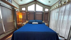 A bedroom with a large bed, a nightstand, a lamp, and a window with blinds.