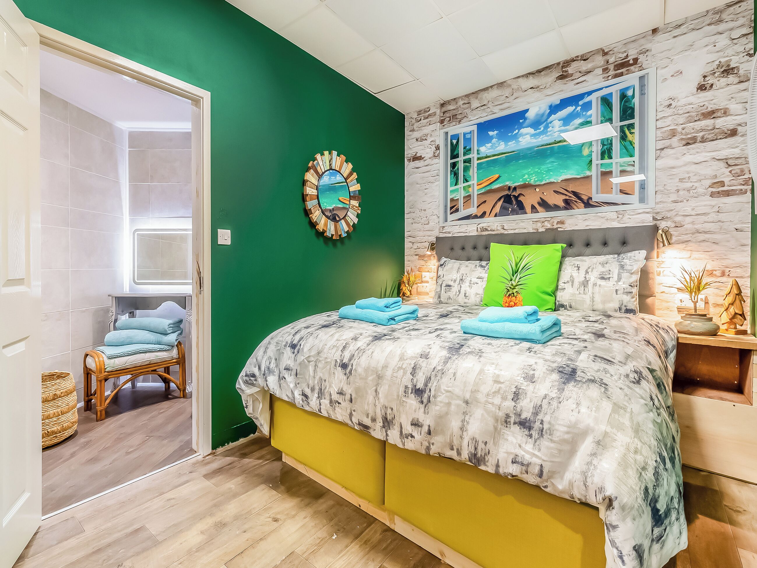 Een slaapkamer met een bed, een groene wand, een strandschildering en een rieten stoel.