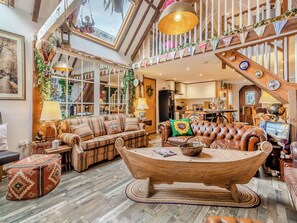 A spacious living area with a large wooden coffee table, leather sofas, and a high ceiling with a skylight. - 2 bedroom accommodation in Beccles (Beccles)