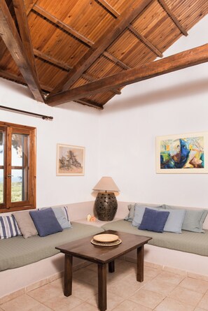 Une pièce avec un plafond en bois, un canapé avec des coussins bleus, une table avec une lampe, et deux œuvres d’art encadrées accrochées au mur.