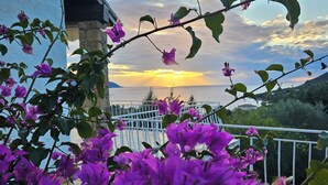 Un balcón con flores moradas y vista al atardecer sobre el mar.