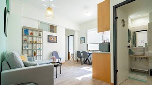 A modern living room with a sofa, chairs, a dining area, and a kitchen with a sink and microwave. - Athenais 3A 2 bedroom 4 persons apartment by MPS (Athina)