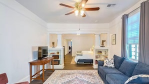 A modern living room with a ceiling fan, a sofa, a desk, and a bookshelf. - 1 block to Trolley, Short walk to Historic Cemeteries, Clean, Coffee Bar (New Orleans)