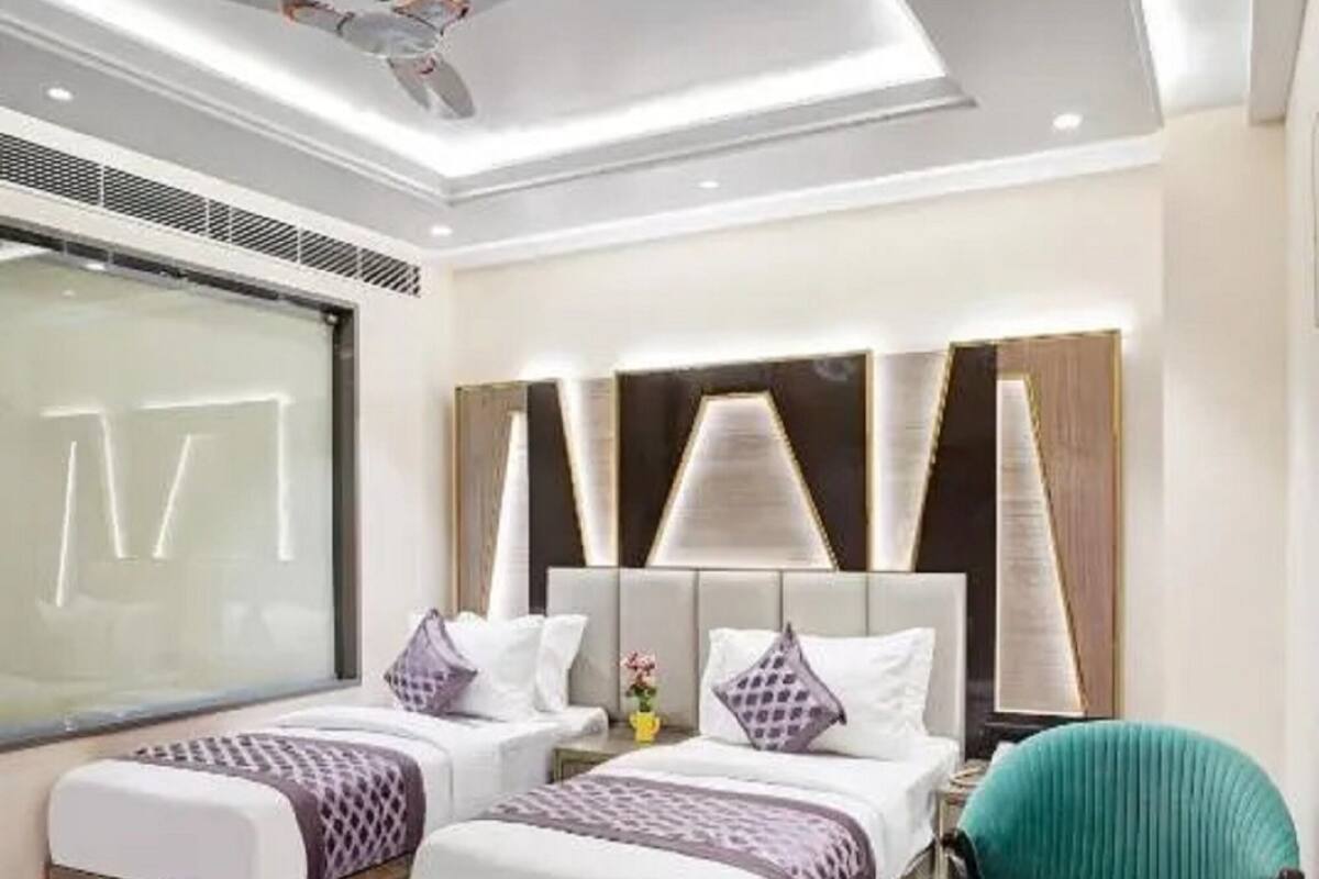 A modern hotel room with two beds, a ceiling fan, and a dining area with a table and chairs.