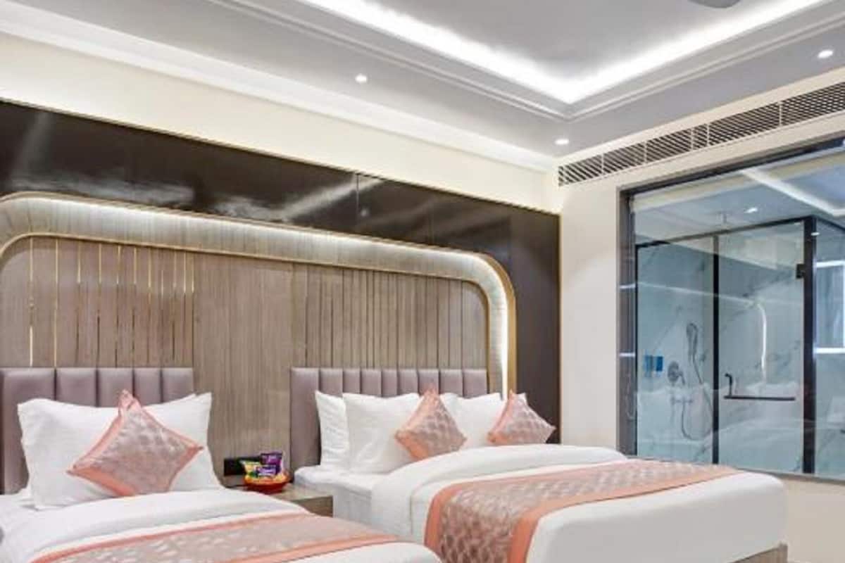 A modern hotel room with two beds, a glass shower enclosure, and a fruit bowl on a glass table.