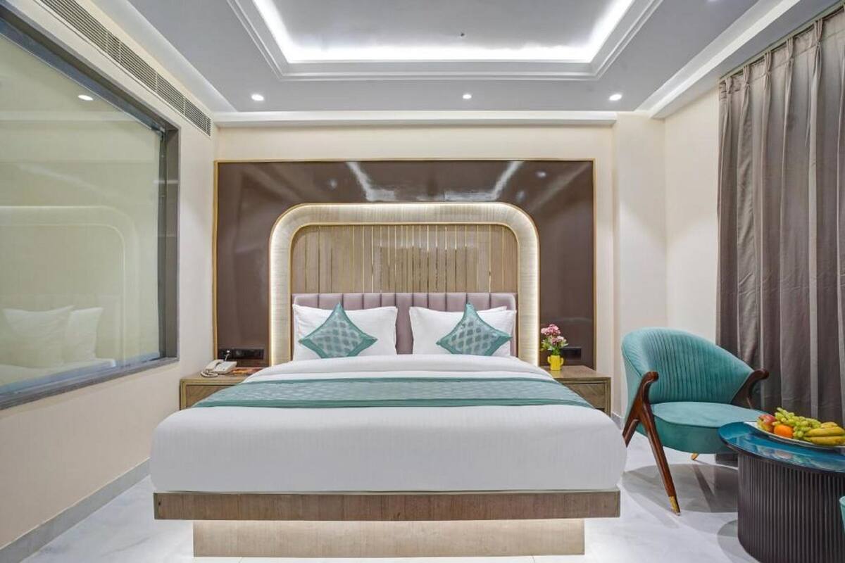 A modern hotel room with a large bed, a nightstand, a teal armchair, and a small table with fruit.
