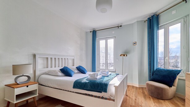 Une chambre à coucher avec un lit, une table de chevet, une chaise et une vue sur la ville par la fenêtre.