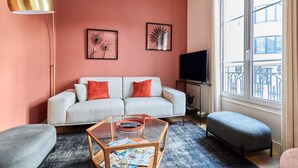 Un salon comprenant un canapé, un pouf, une table basse et un lampadaire.