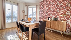 Un coin repas avec une table en bois, des chaises noires et un mur orné d’un motif.