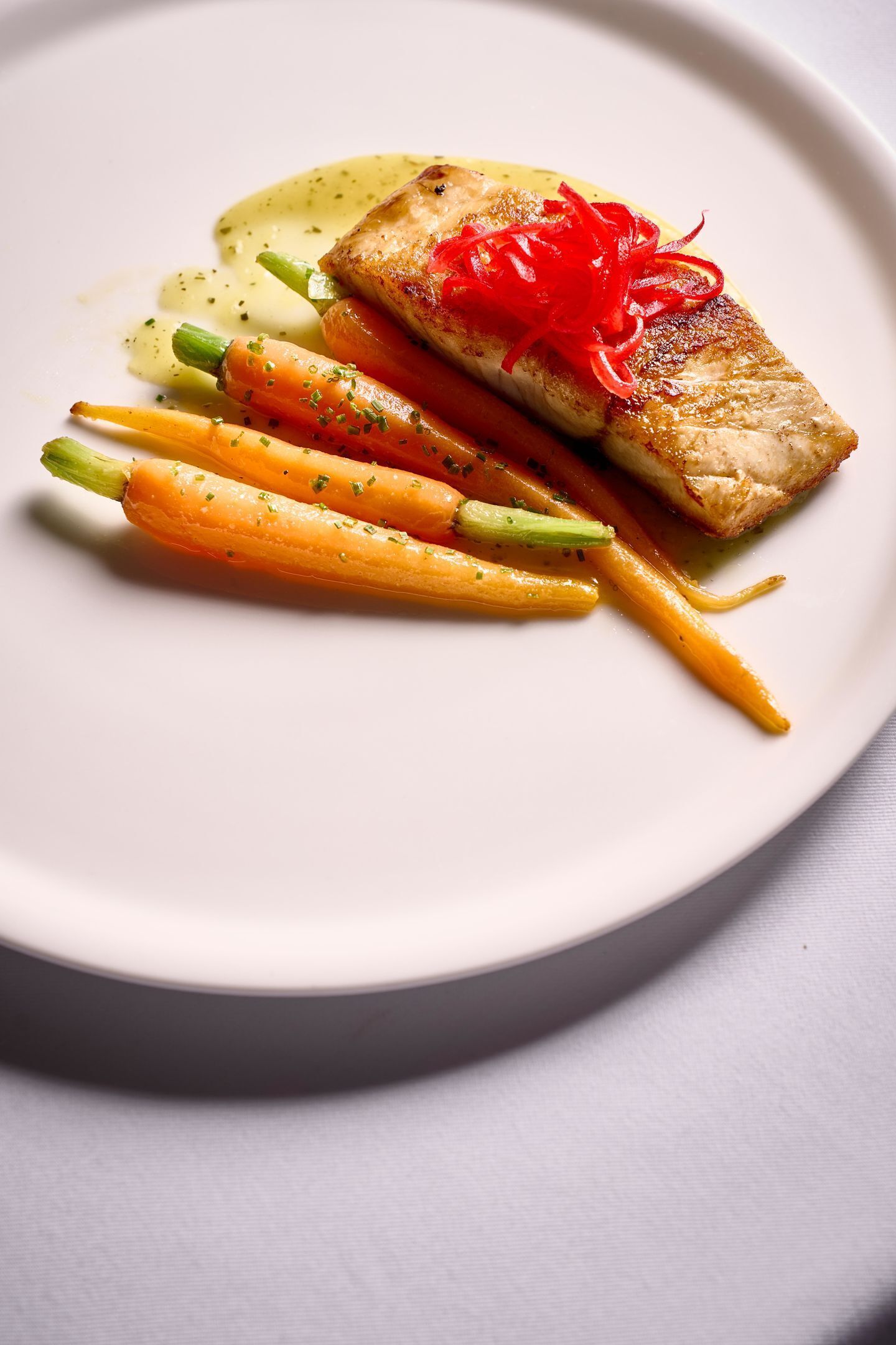 A plate with a piece of grilled fish, asparagus, and carrots, garnished with red strips.