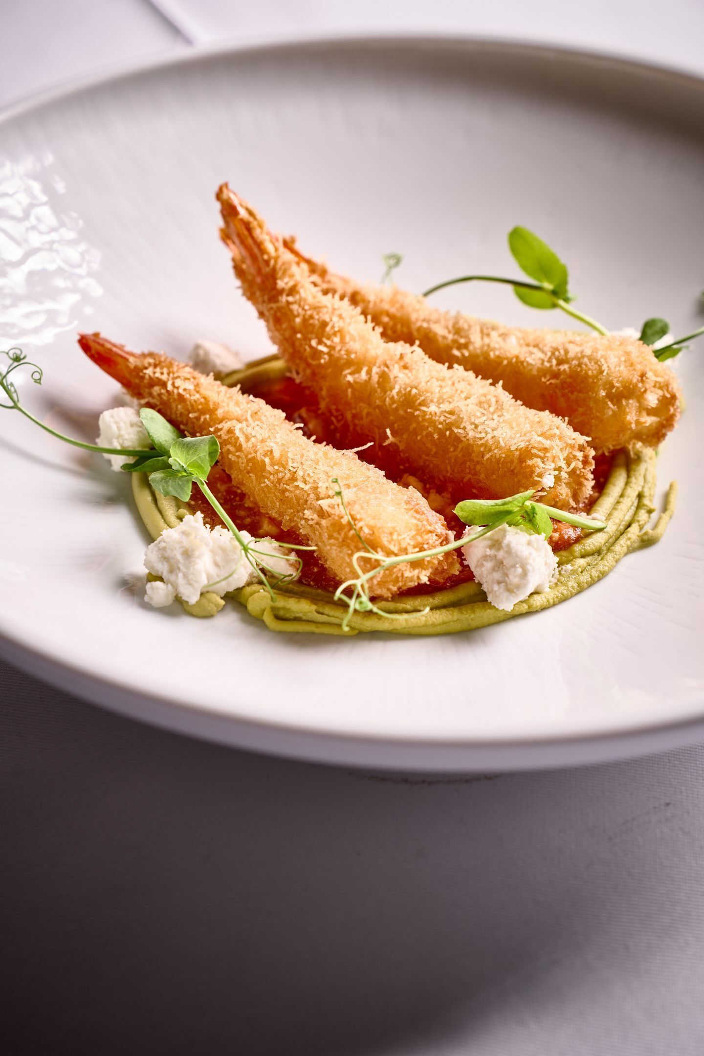 A plate with breaded shrimp, greens, and a dollop of cream.