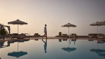 A pool area with lounge chairs and umbrellas, a person walking, and a clear sky.