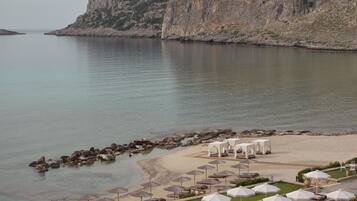 Un resort frente a la playa con sillas de sol, sombrillas y un acantilado rocoso al fondo.