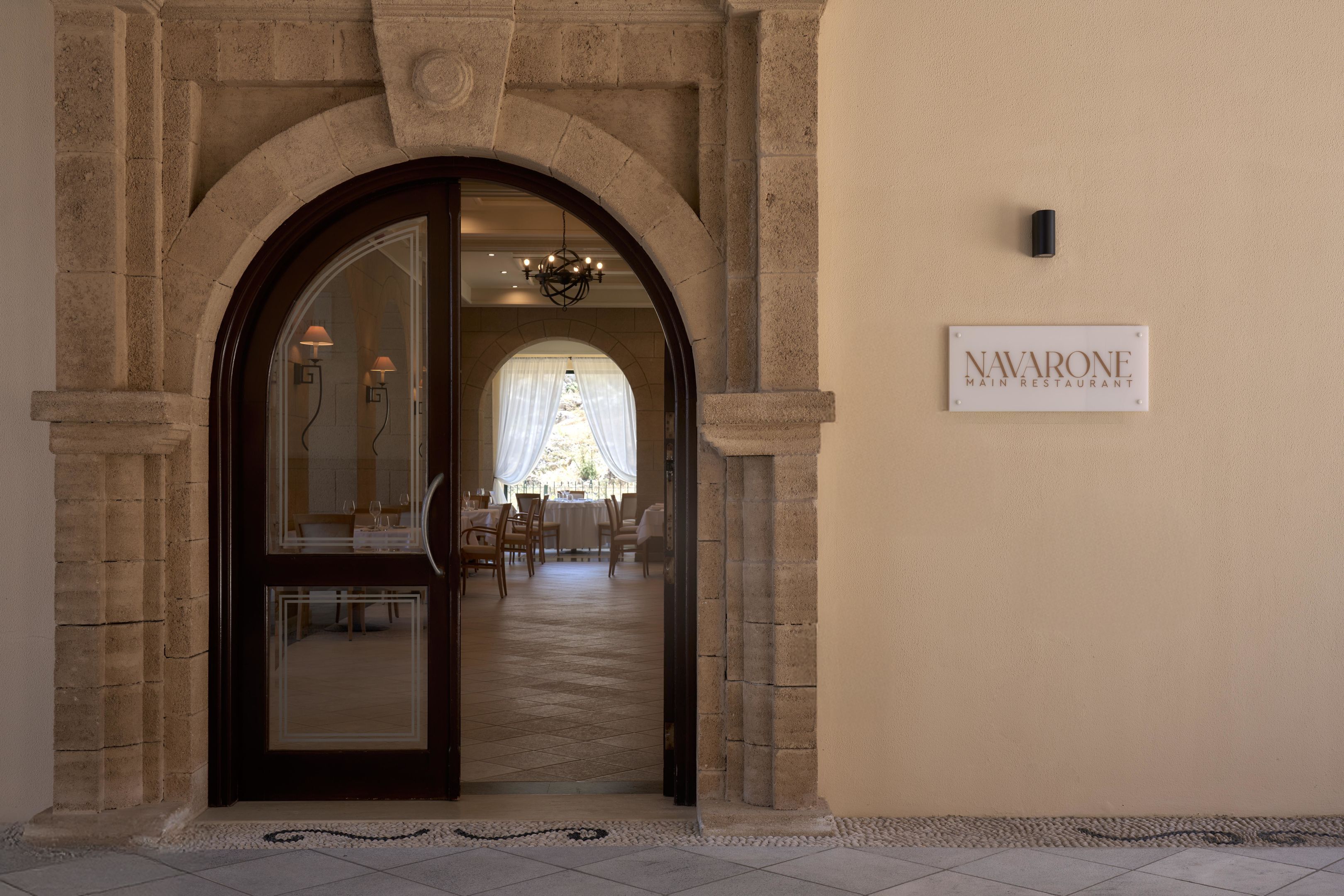Een ingang naar Navarone Main Restaurant met een stenen boog, een bord boven de deur en een zicht op de eetzaal.