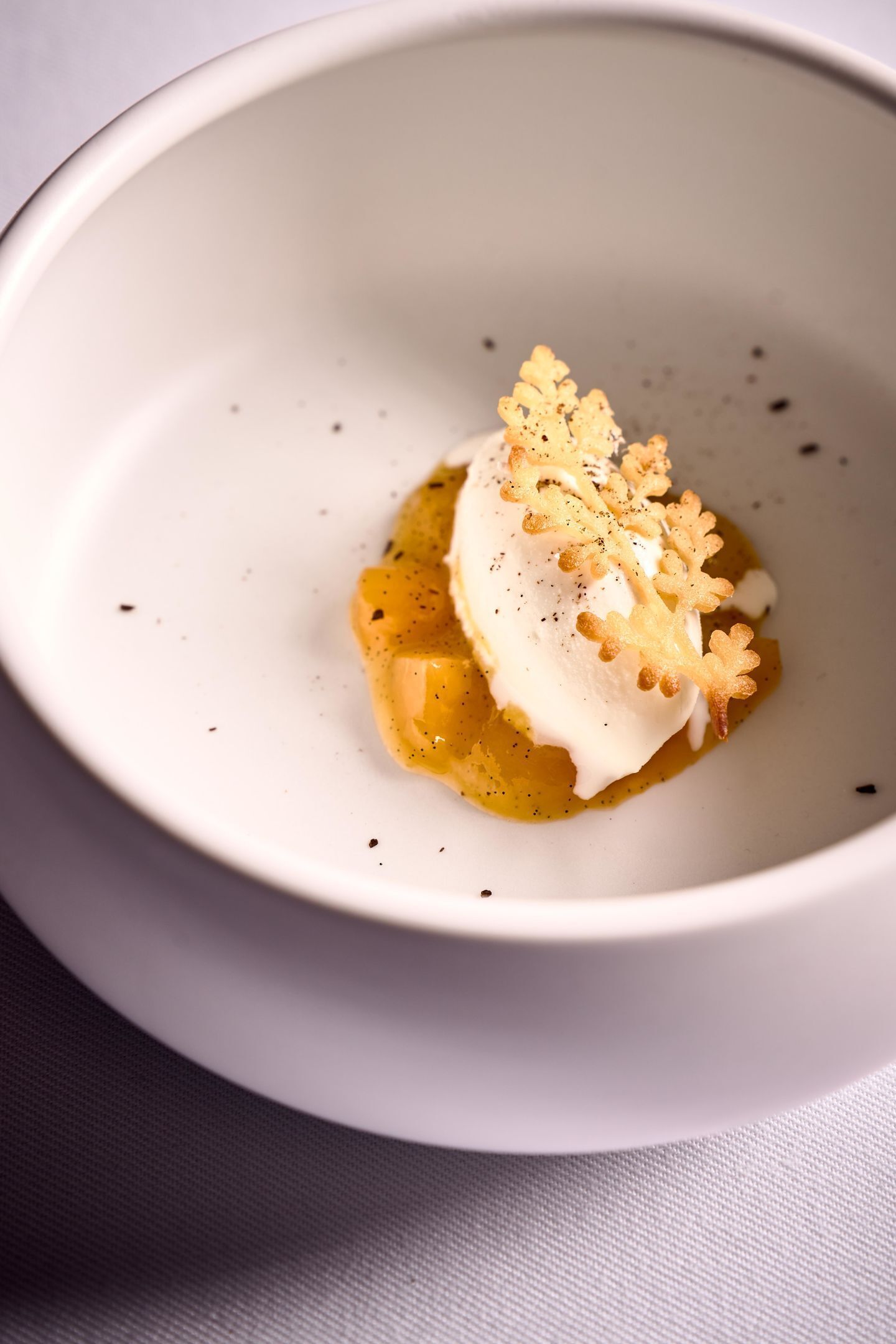 Un tazón blanco con un postre y cobertura cremosa, decorado con un adorno dorado.