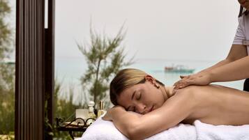 A person receiving a back massage outdoors with a view of the sea and greenery in the background.