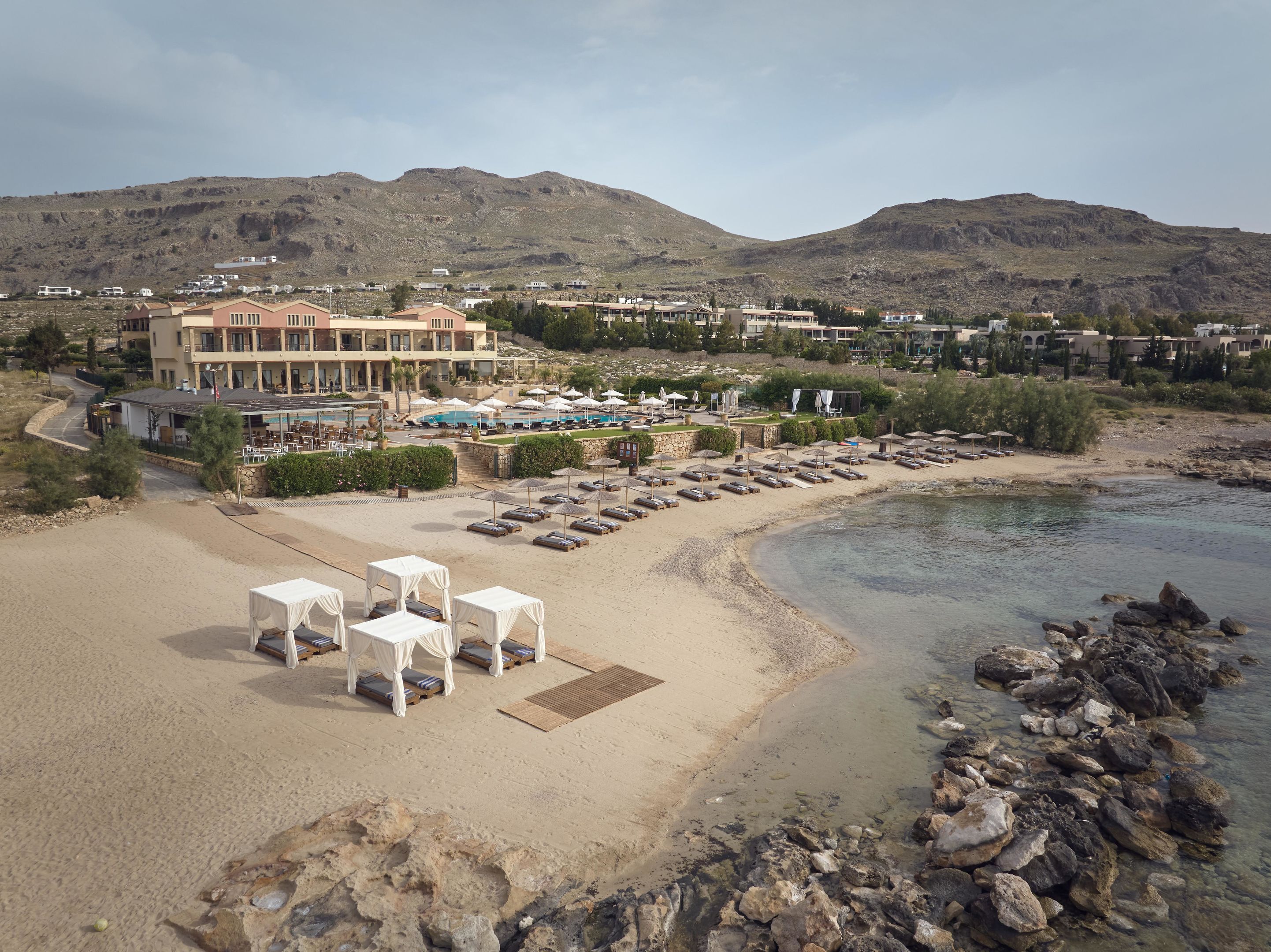 Un hotel frente a la playa con piscina, sillas y sombrillas.