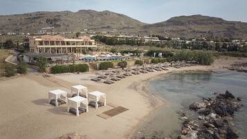Un hotel frente a la playa con piscina, sillas y sombrillas.