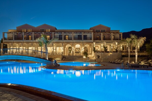 A large, multi-story hotel with a swimming pool, outdoor seating, and a well-lit entrance. - Lindian Dream Seaside Resort (Lindos)