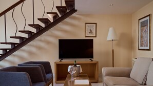 Una sala de estar moderna con una escalera de madera, un televisor de pantalla plana, un sofá y una mesa de centro con una botella y una copa.