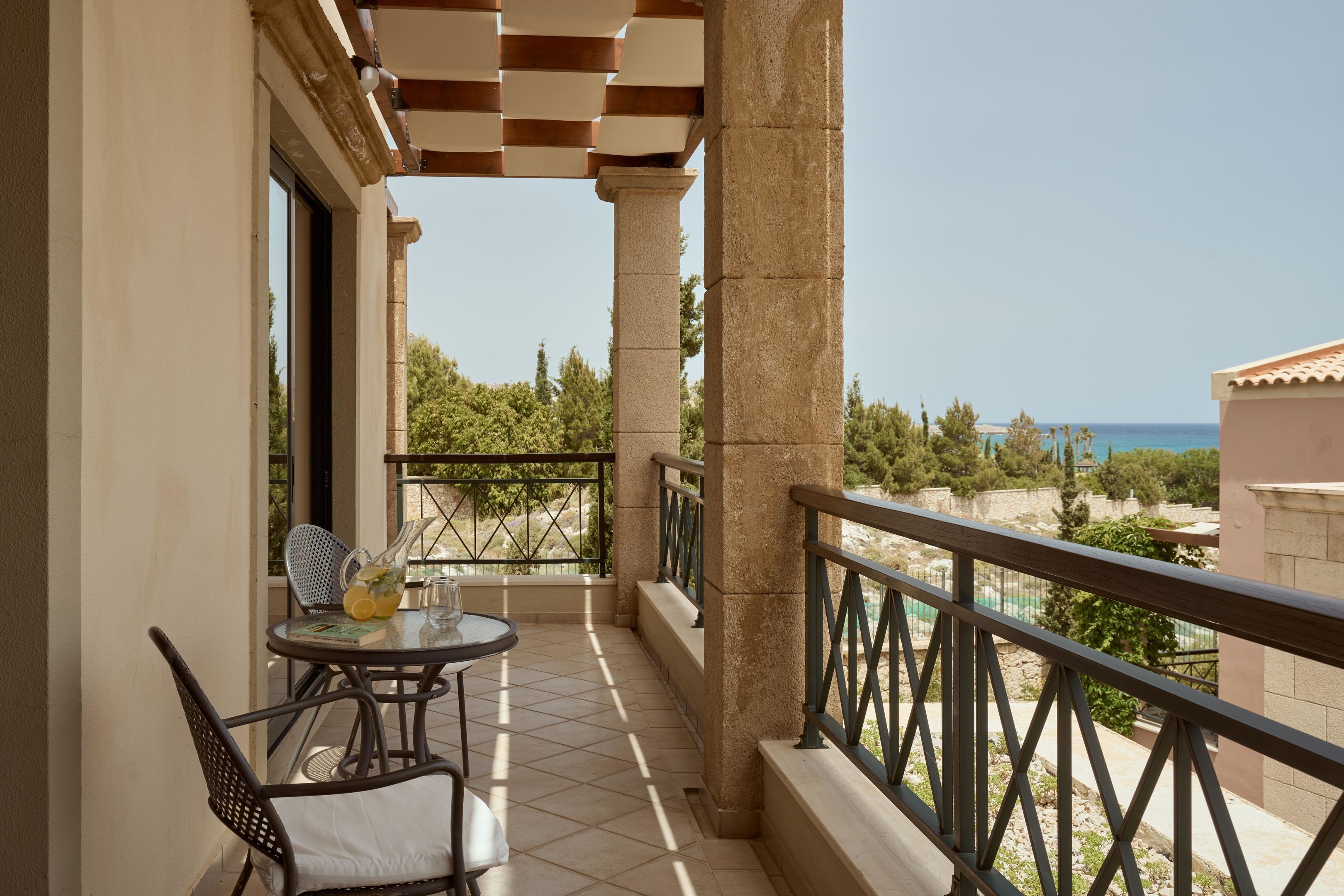 A balcony with a table and chairs, a view of the sea, and a tiled floor.
