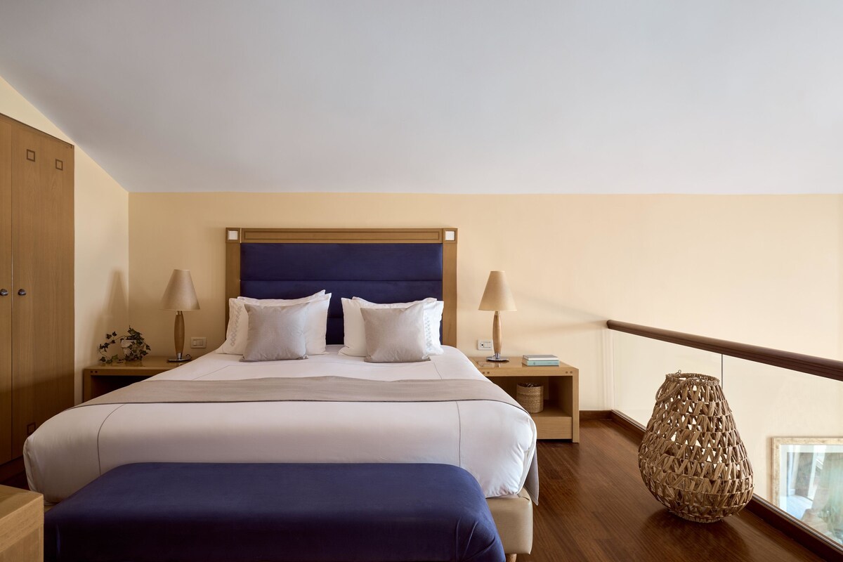 Una habitación de hotel con una cama grande, dos mesitas de noche, un armario de madera y un jarrón decorativo.