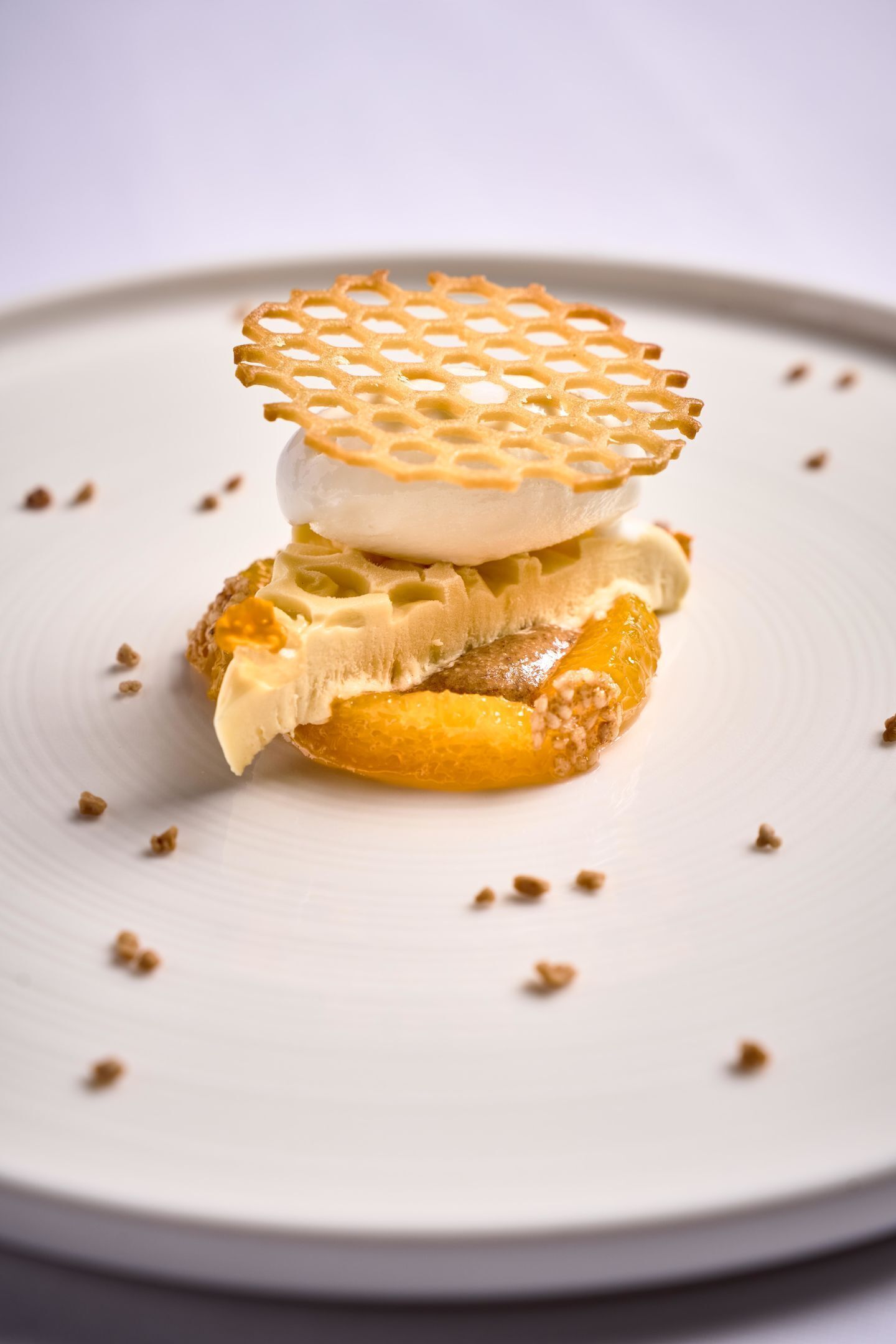 A dessert on a white plate with a lattice top, a slice of orange, and a creamy layer.