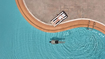 Vista aérea de una piscina de borde curvo, un área de descanso con una silla a rayas y un trampolín.