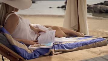 A person reading a book on a beach chair with a view of the sea and rocks.
