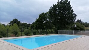 A rectangular swimming pool with tiled edges, surrounded by a fence and trees.