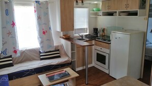 A compact kitchen with a dining area, a small refrigerator, and a window with curtains.