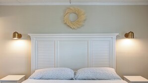 Une chambre à coucher avec une tête de lit blanche, deux tables de chevet et un luminaire fixé au mur.