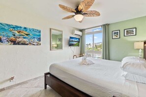 A bedroom with a bed, a ceiling fan, a TV, and a large window. - Partial oceanview 1 bedroom condo, AC, 6 mile sandy beach (Kihei)