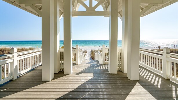 Une promenade en bois mène à une plage où se trouve un kiosque blanc.